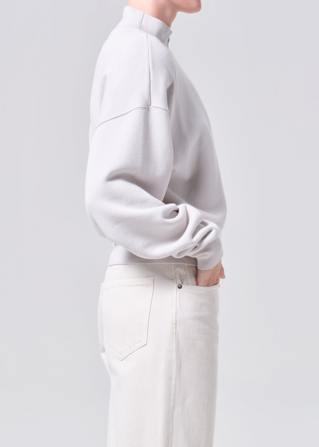 Person wearing a light gray sweater and white pants on a plain background