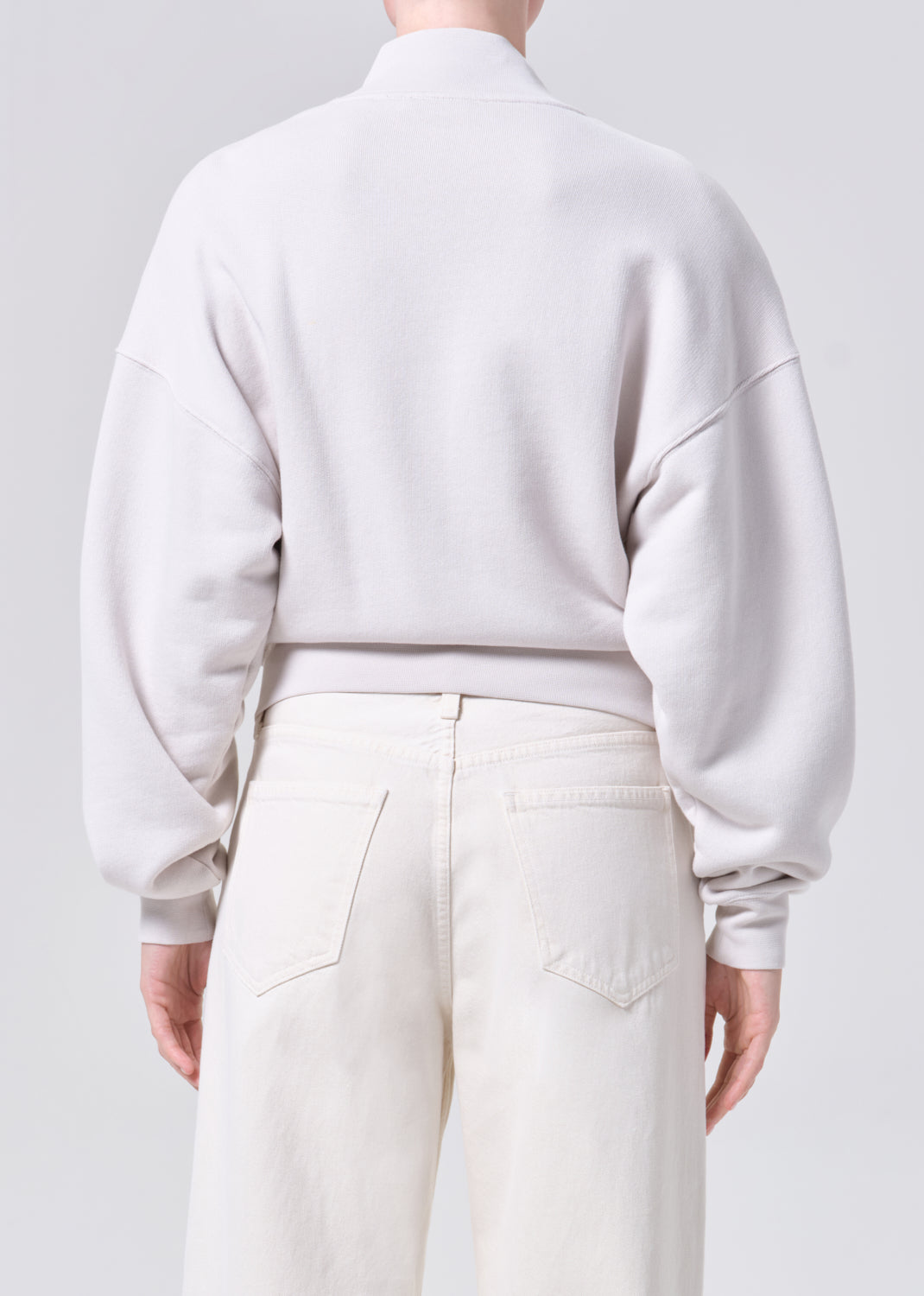 Person wearing a light gray sweatshirt and white pants against a plain background