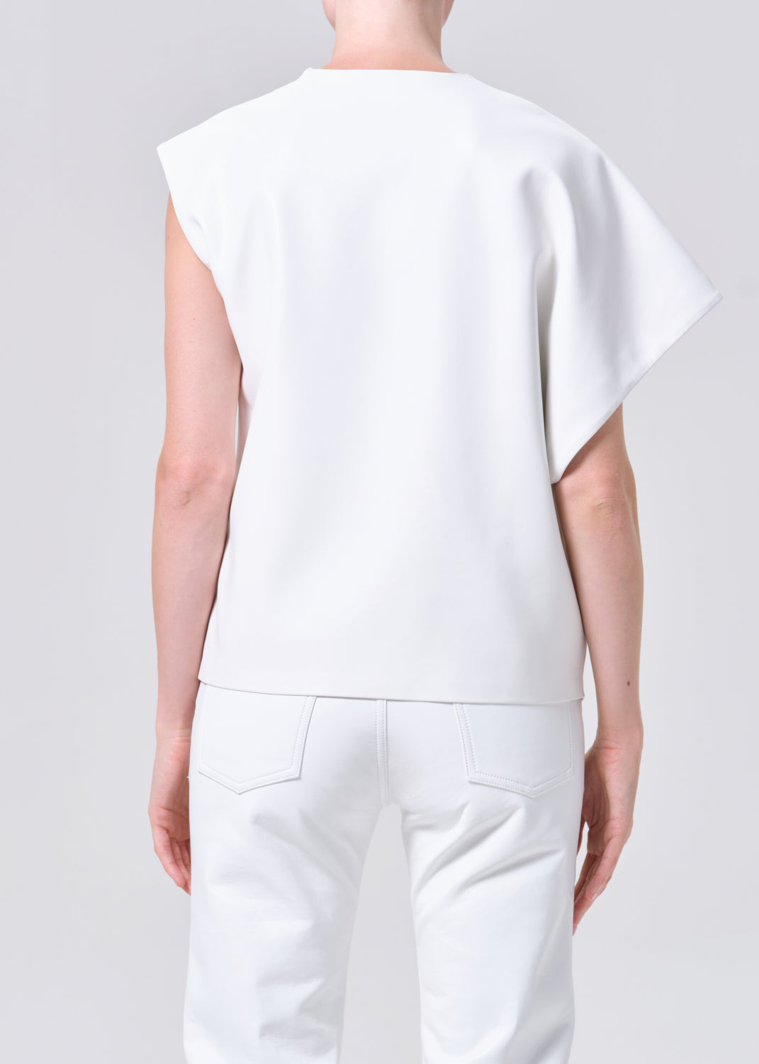 Person wearing a white sleeveless top and pants on a light gray background