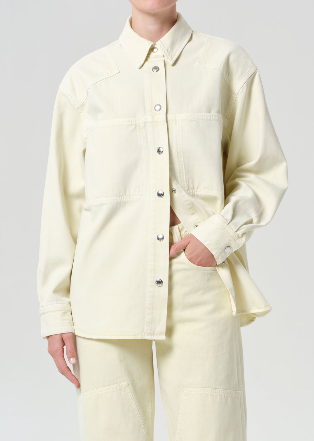 Person wearing a light yellow button-up shirt and pants on a plain background