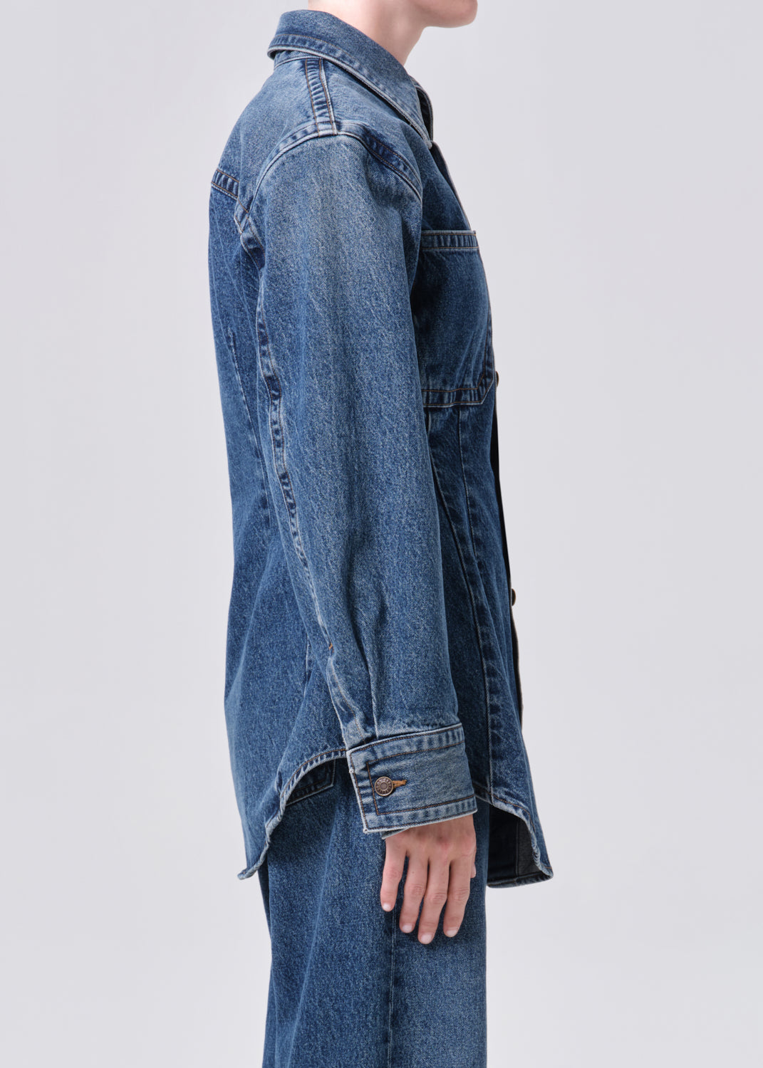 Person wearing a long blue denim jacket on a light gray background
