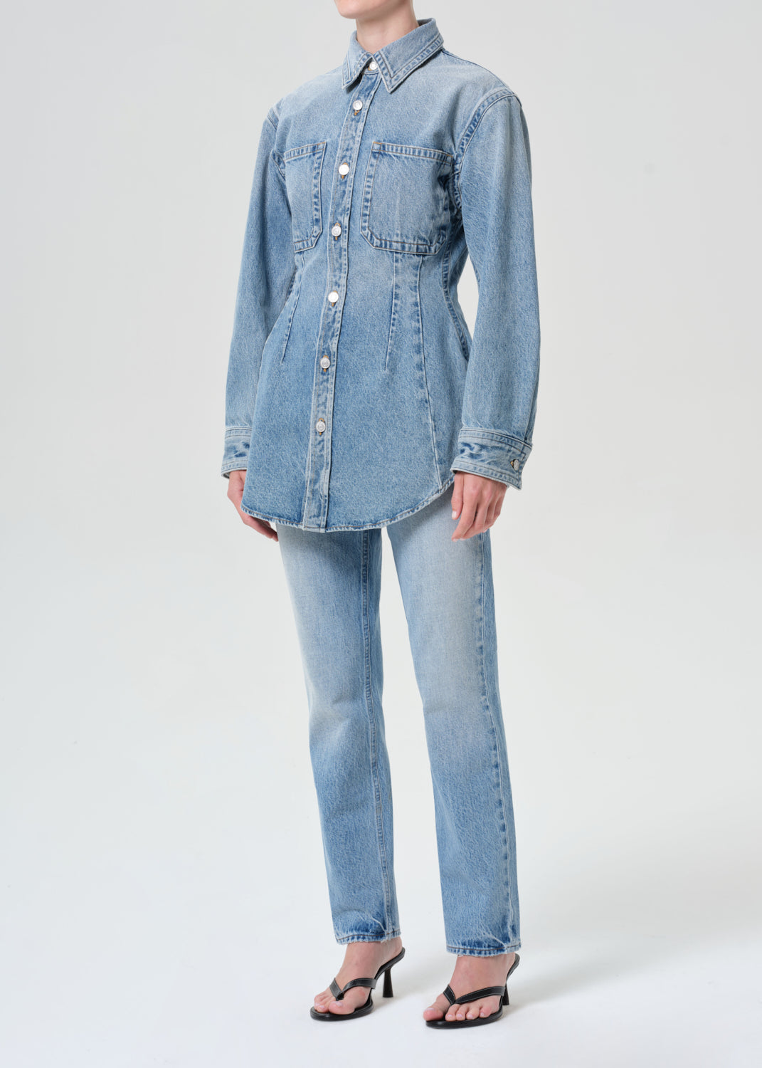 Person wearing a light blue denim shirt and jeans on a white background