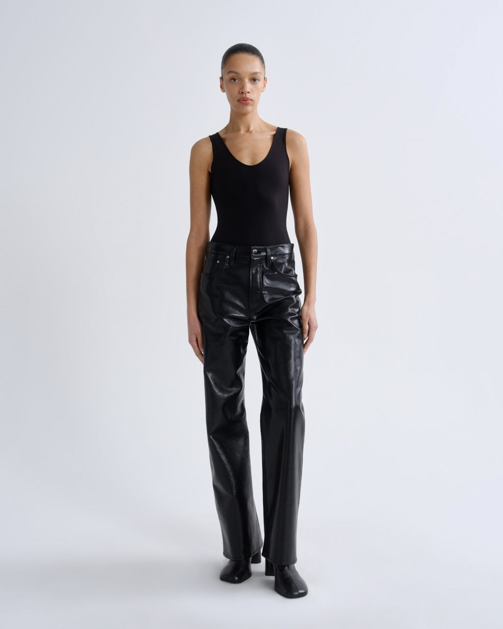 Person wearing a black tank top and black leather pants on a white background