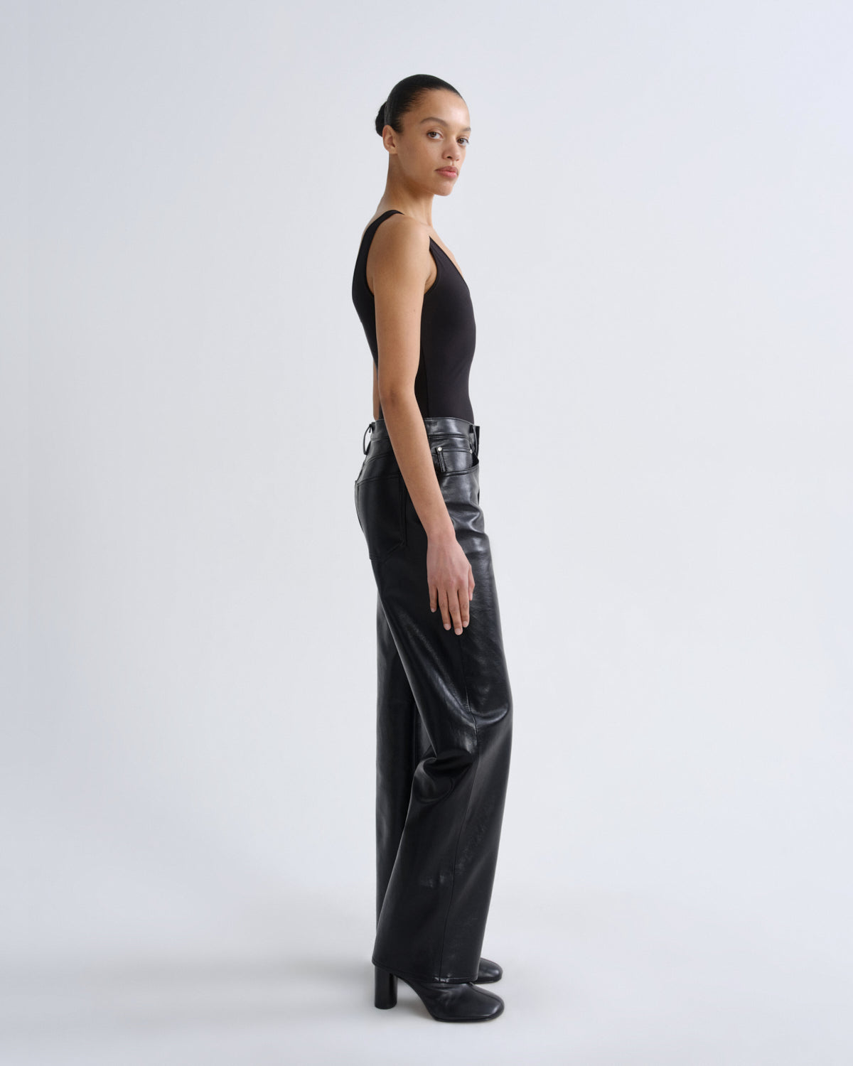 Person wearing black sleeveless top and shiny black pants on a white background