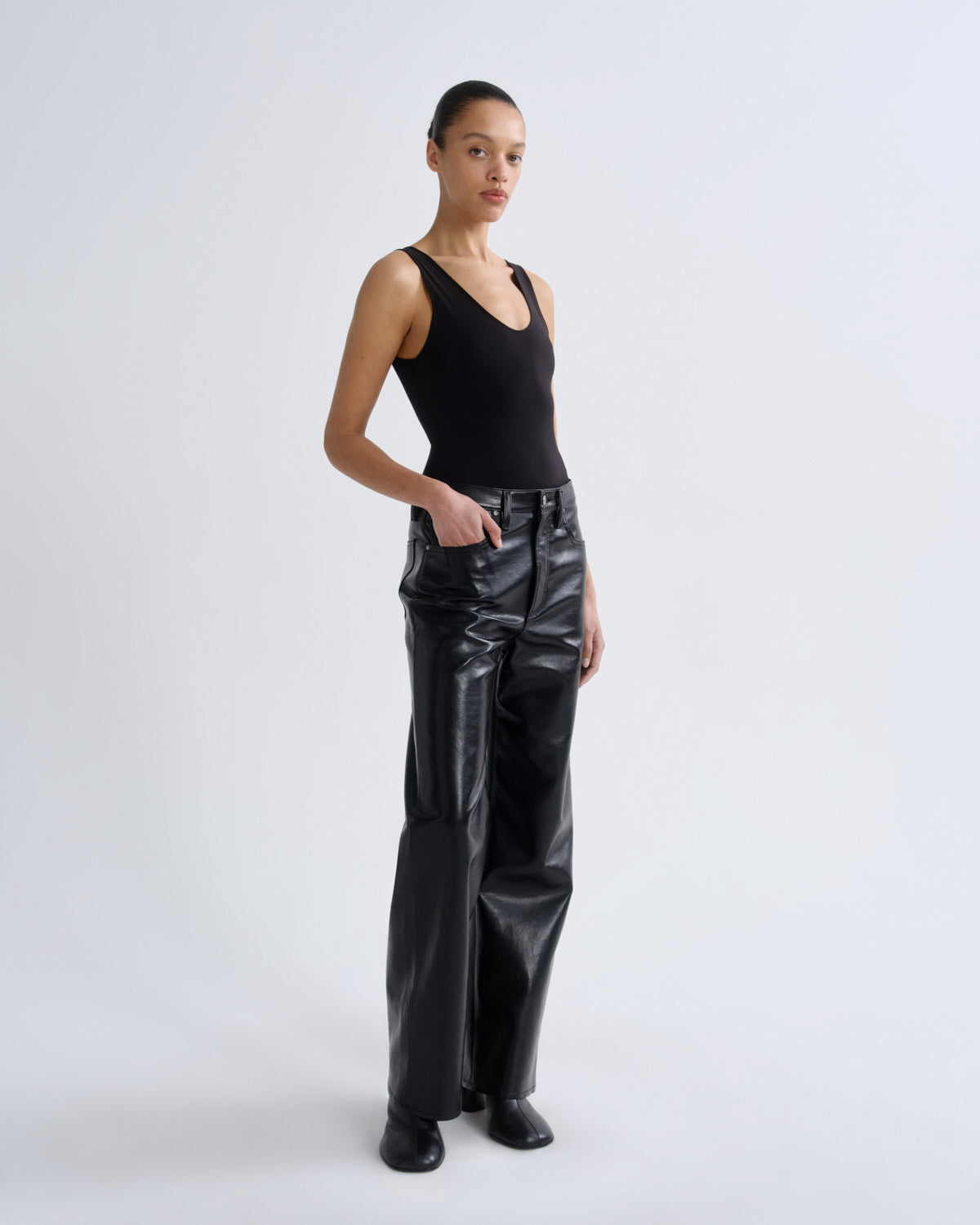 Person wearing black leather pants and a black tank top on a white background
