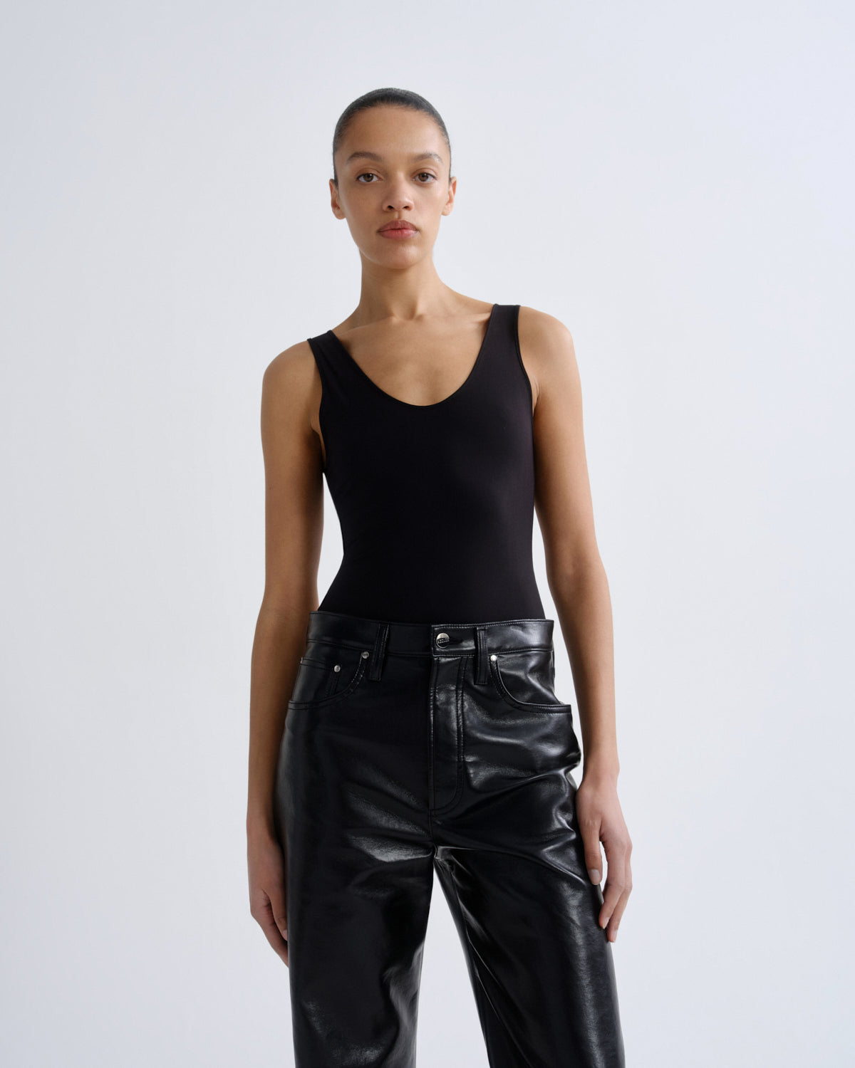 Person wearing a black tank top and black leather pants on a white background