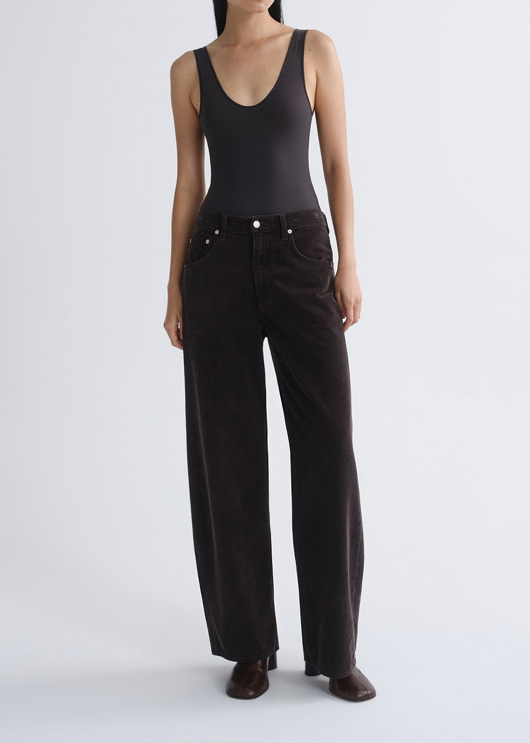 Person wearing a black tank top with black wide leg jeans on a grey background