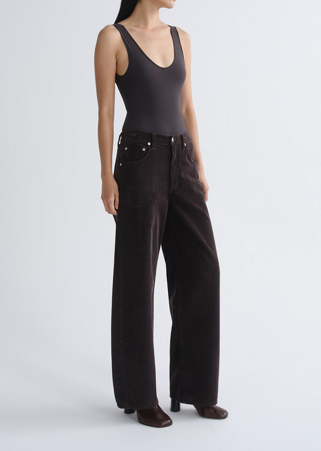 Person wearing a black tank top with black wide leg jeans viewed from the side on a grey background