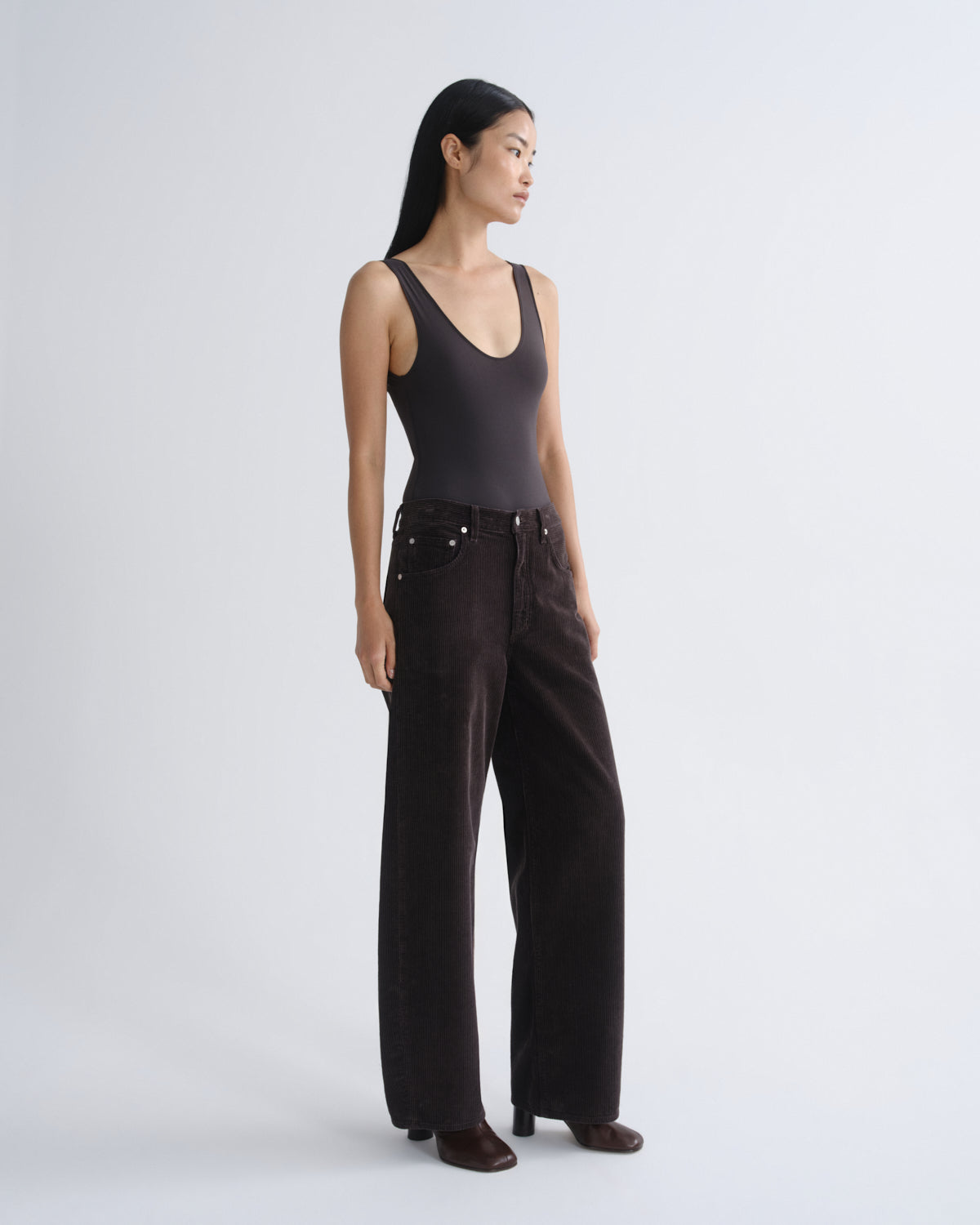 Woman wearing a black tank top and dark pants on a white background