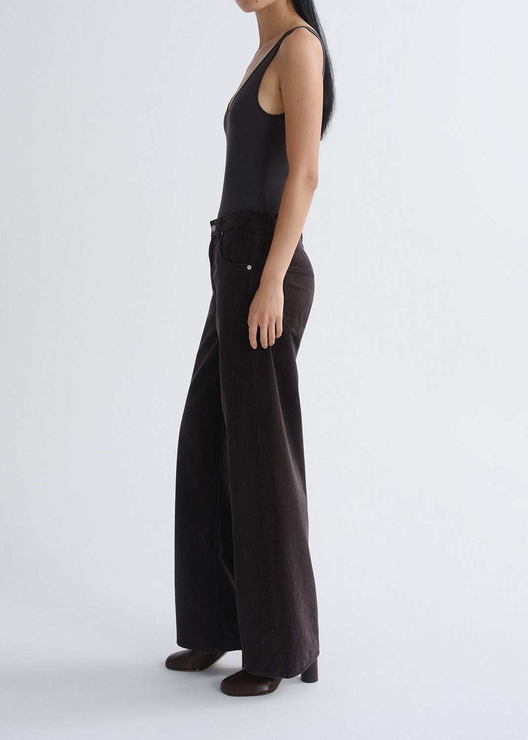 Person wearing a black tank top with black wide leg jeans viewed from the side on a grey background