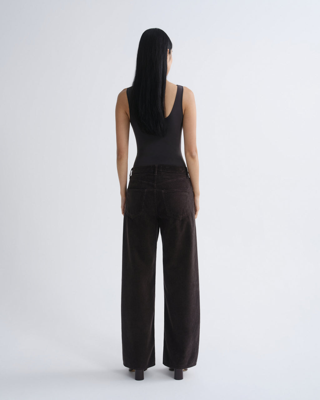Person wearing a black sleeveless top and wide-leg pants on a white background