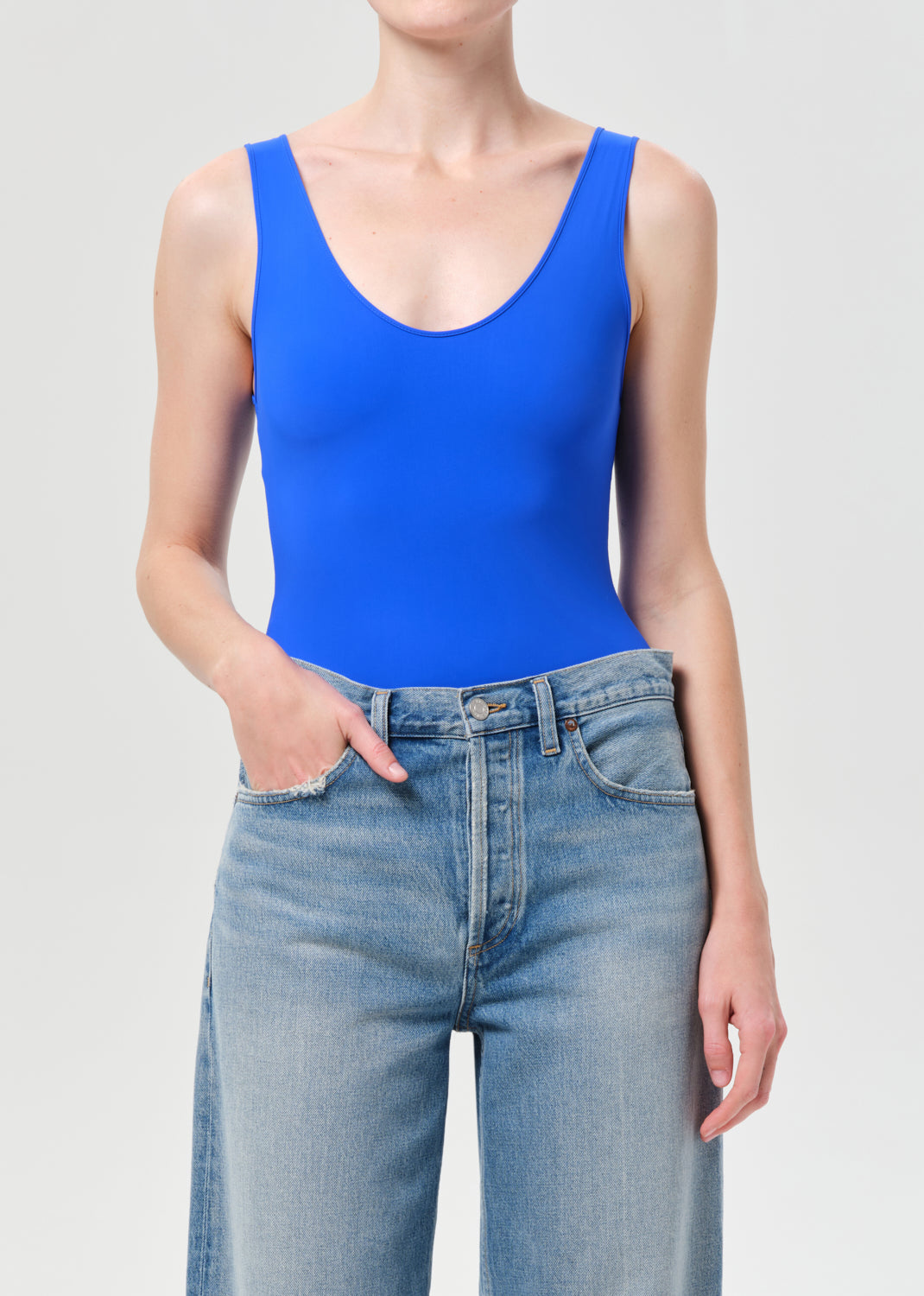 Person wearing a blue tank top and jeans on a plain background