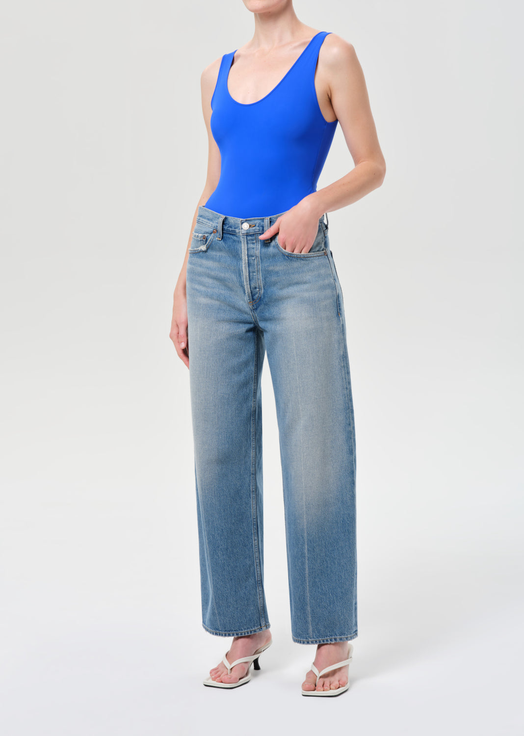 Person wearing a blue tank top and light blue jeans on a white background