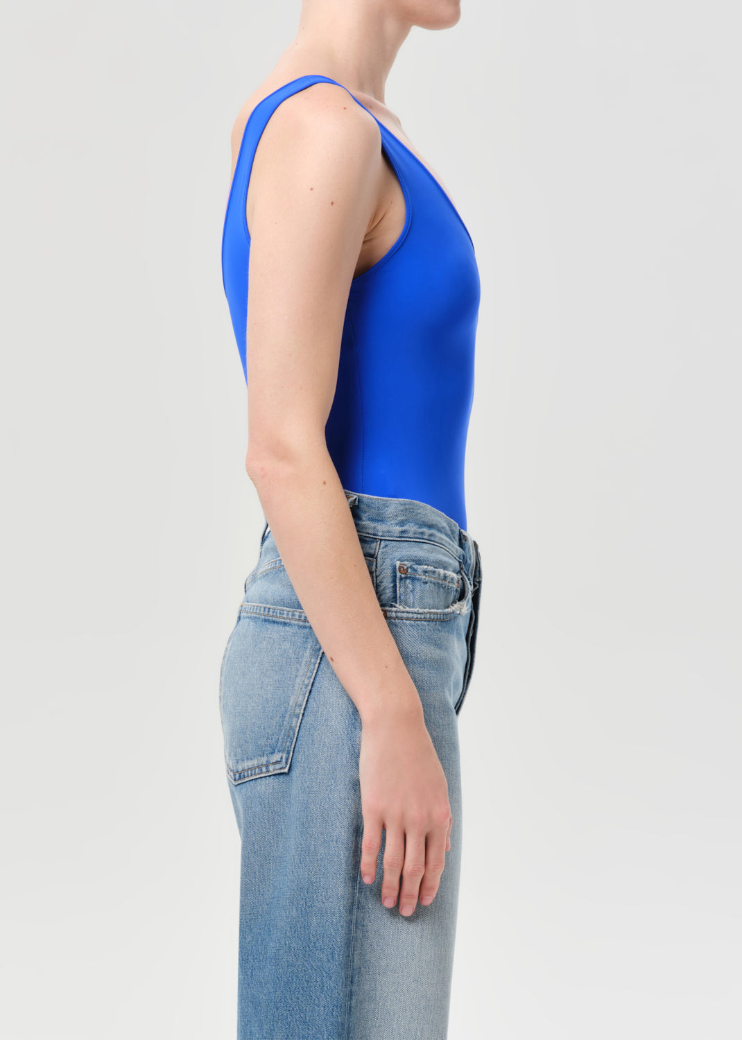 Person wearing a blue sleeveless top and light blue jeans on a plain background