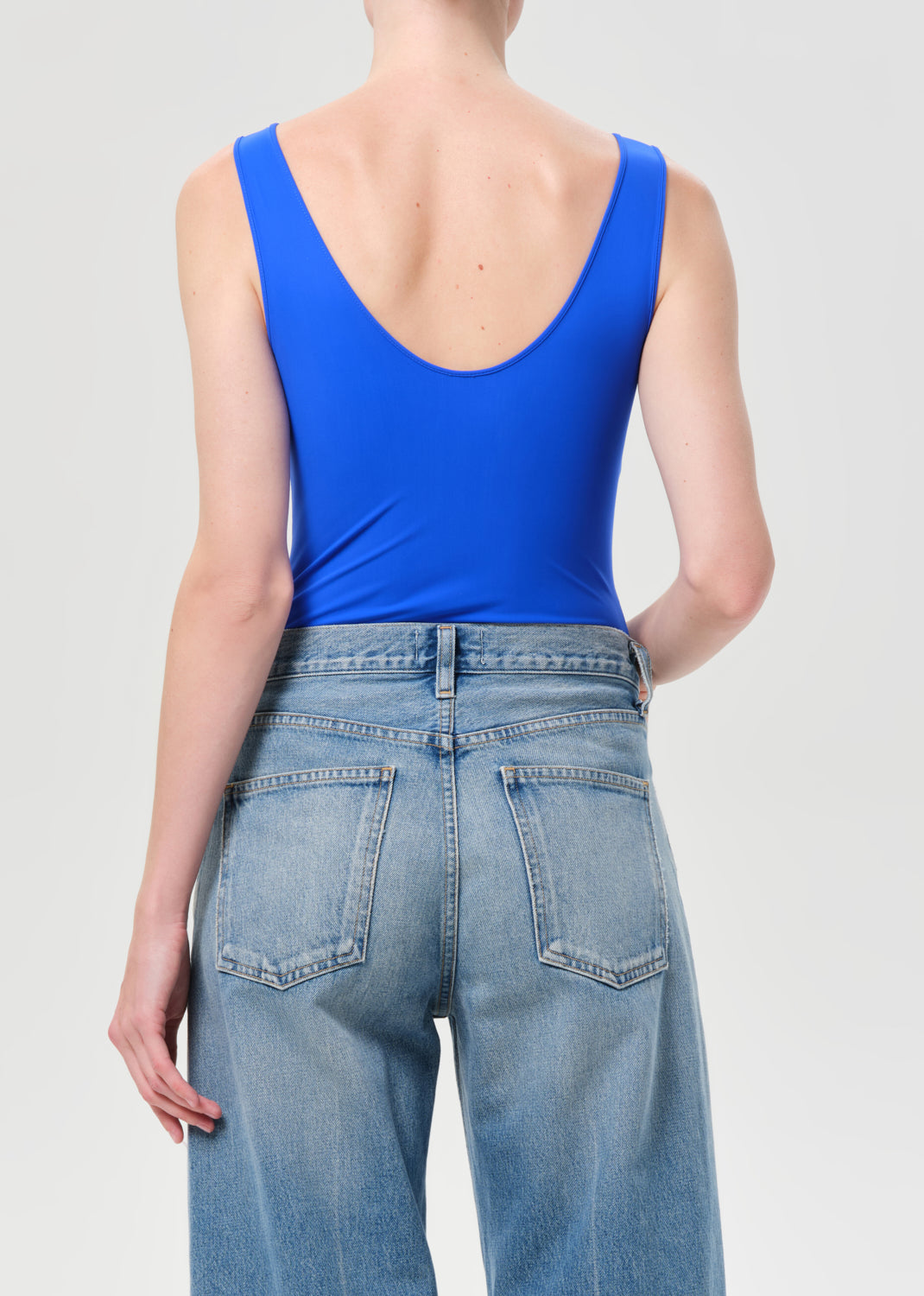Person wearing a blue tank top and light blue jeans on a plain background