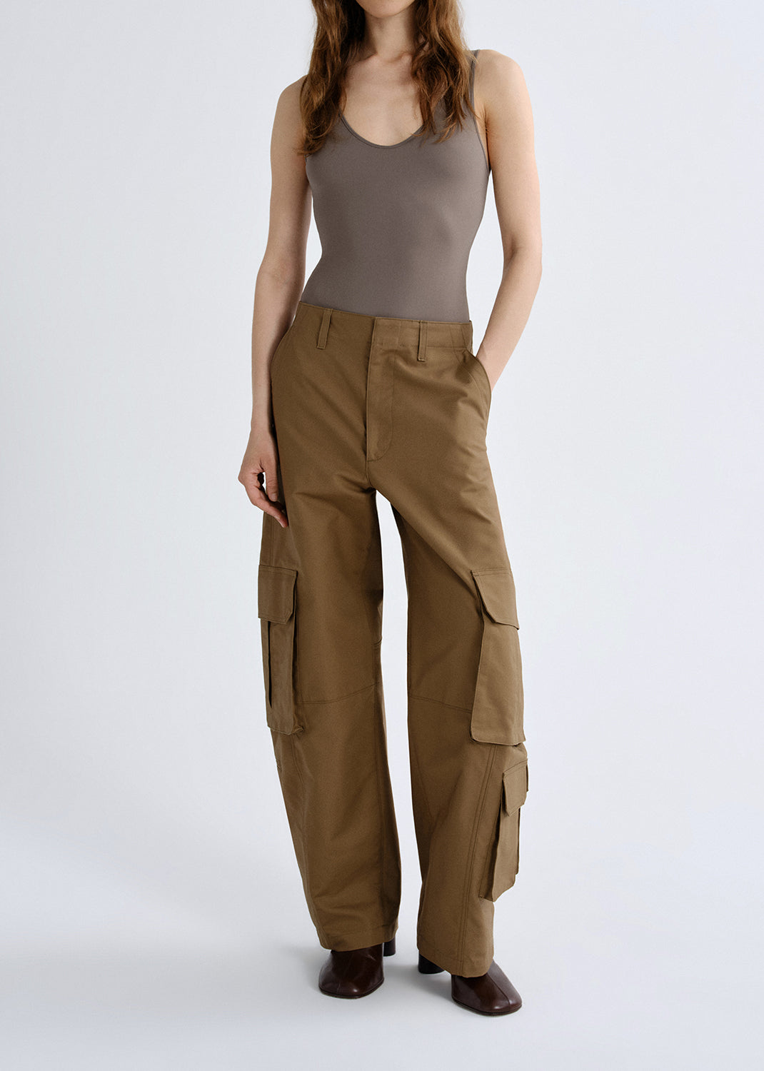 Person wearing a taupe tank top with brown cargo pants on a grey background