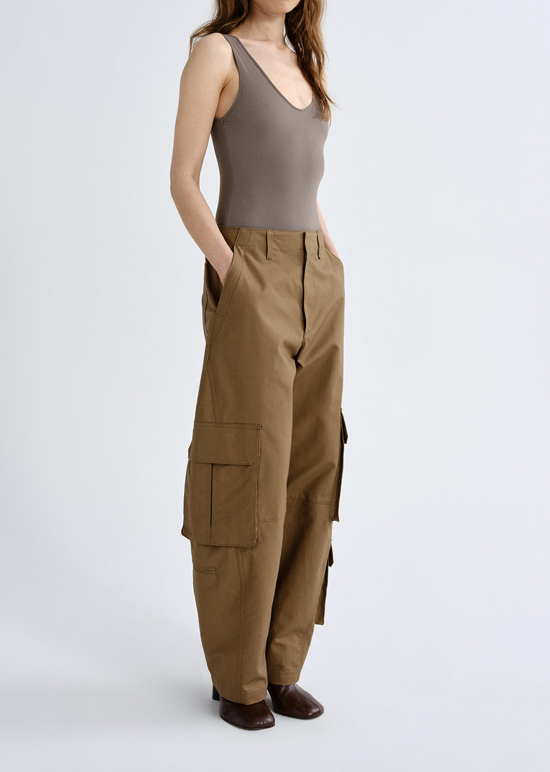Person wearing a taupe tank top with brown cargo pants viewed from the side on a grey background