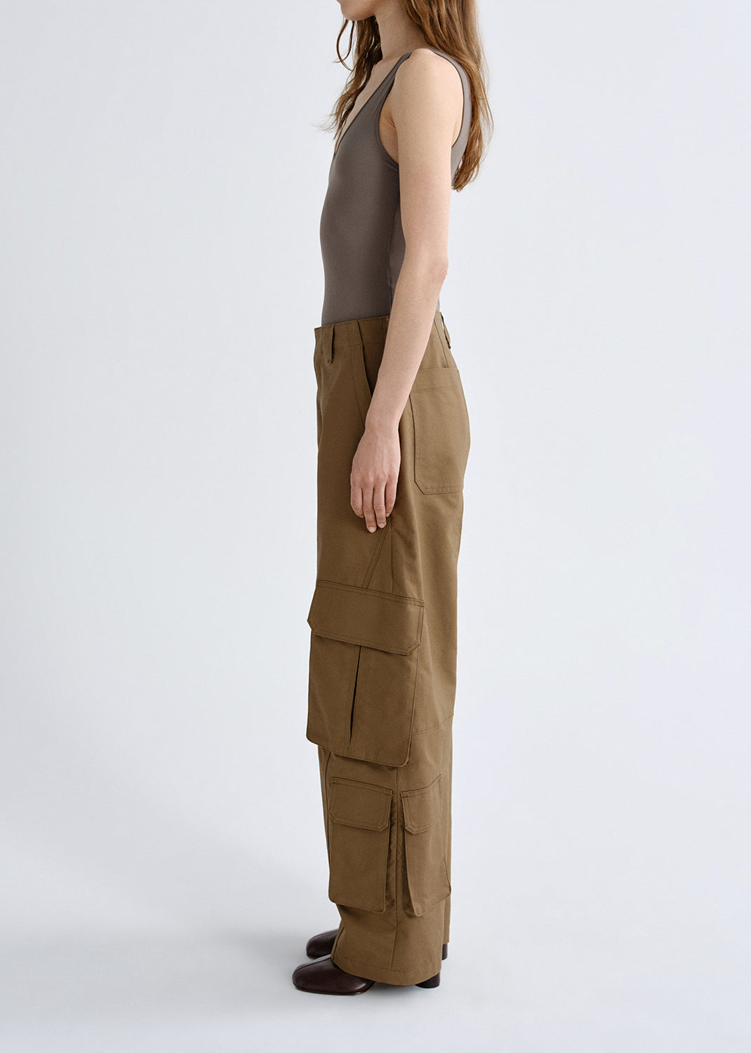 Person wearing a taupe tank top with brown cargo pants viewed from the side on a grey background