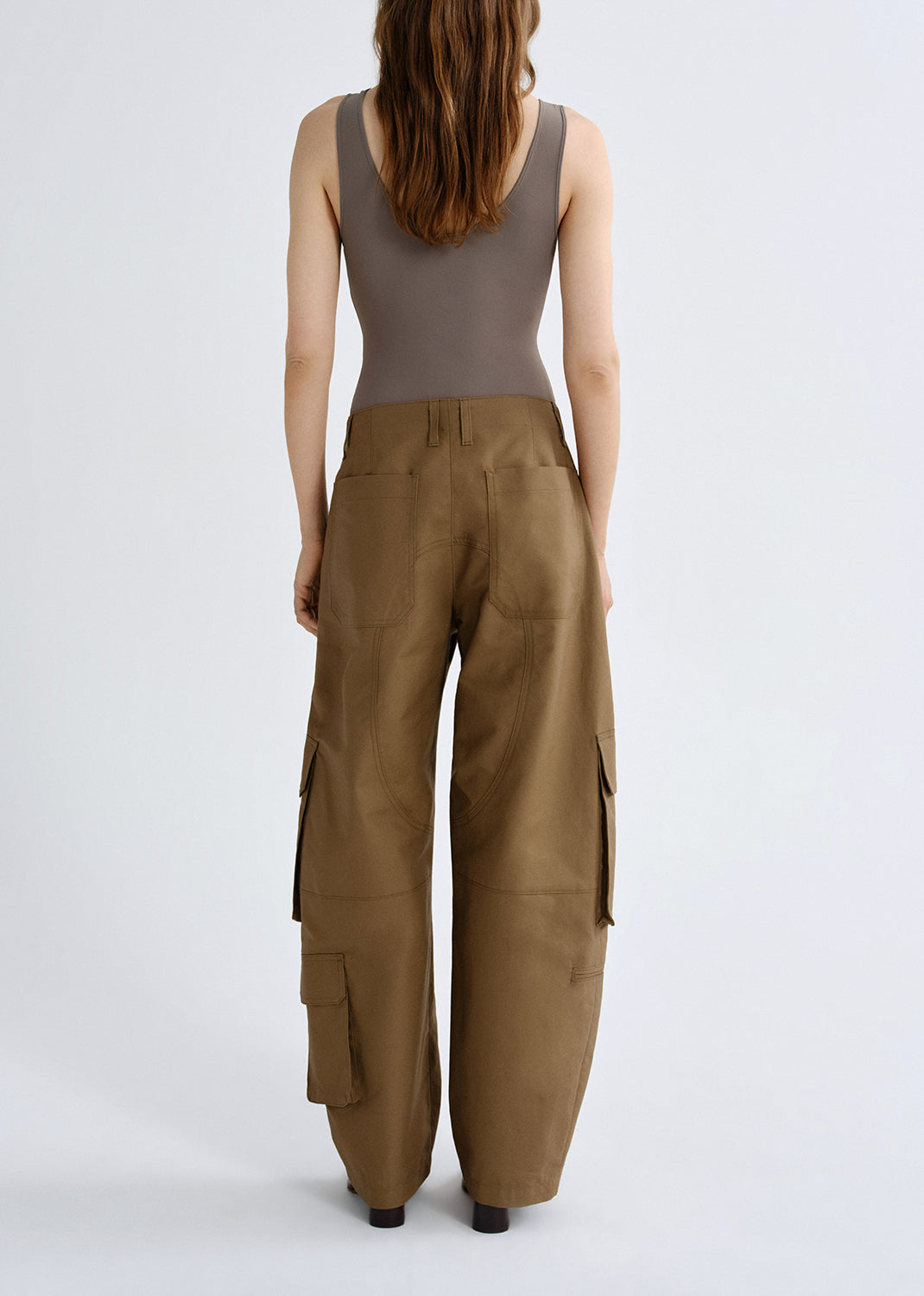 Person wearing a taupe tank top with brown cargo pants viewed from the back on a grey background