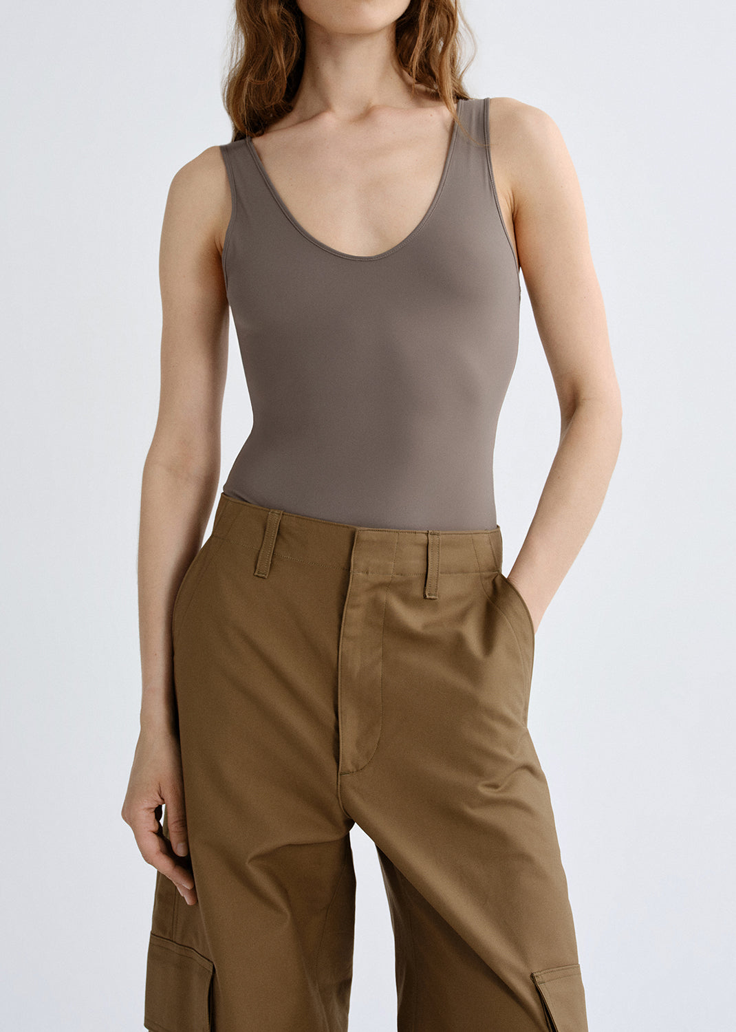 Person wearing a taupe tank top with brown cargo pants on a grey background