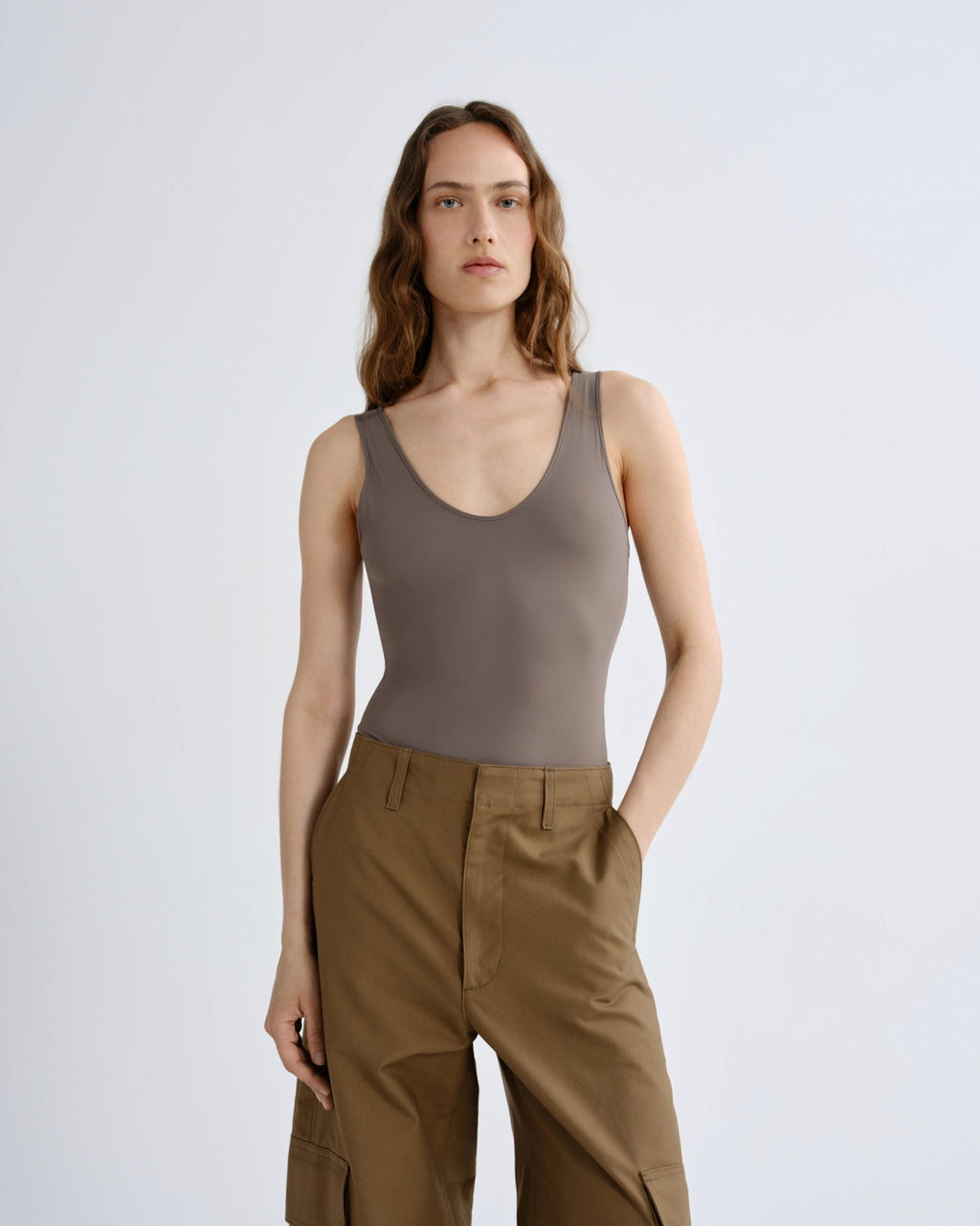 Woman wearing a brown tank top and beige pants on a white background