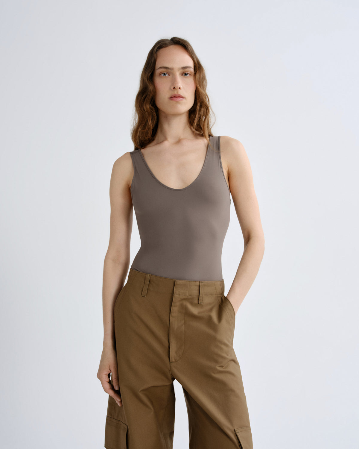 Woman wearing a brown tank top and beige pants on a white background