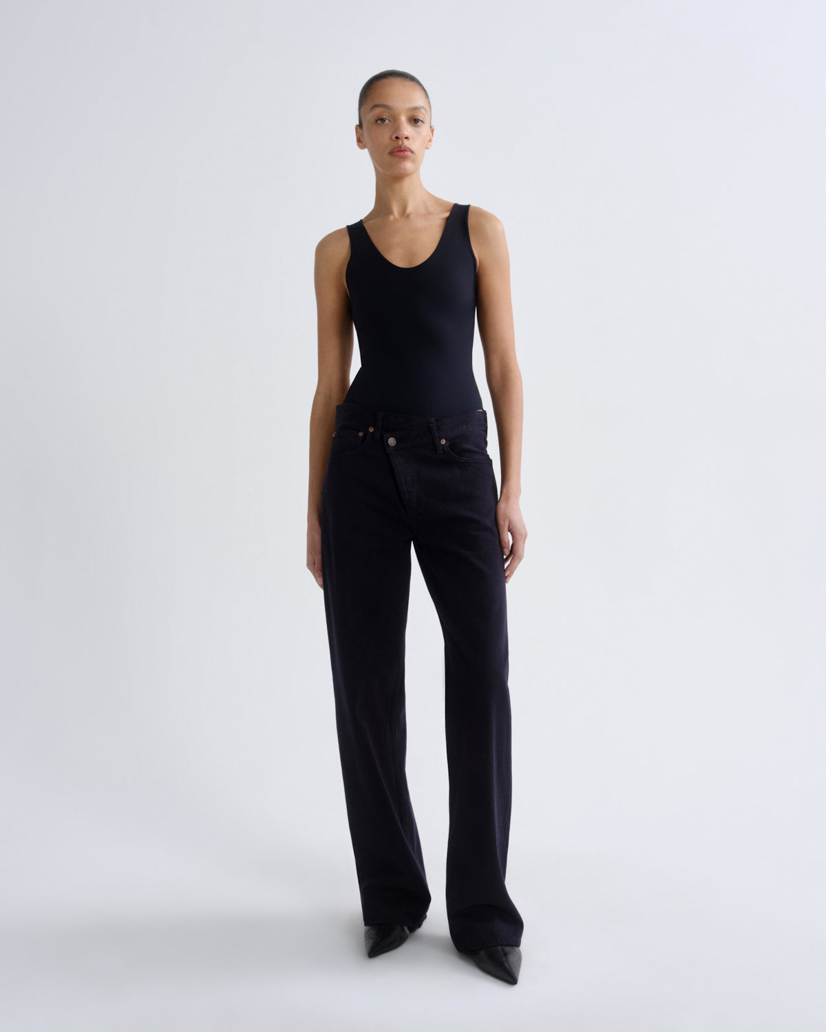 Person wearing a black sleeveless top and black pants on a white background