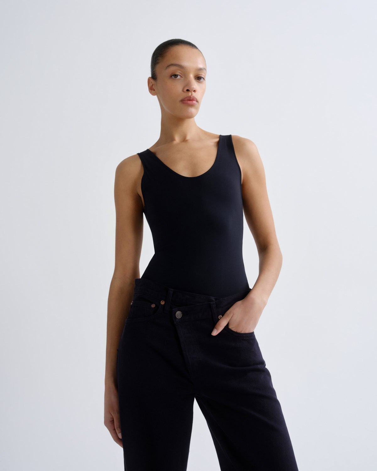 Person wearing a black sleeveless top and black pants on a white background