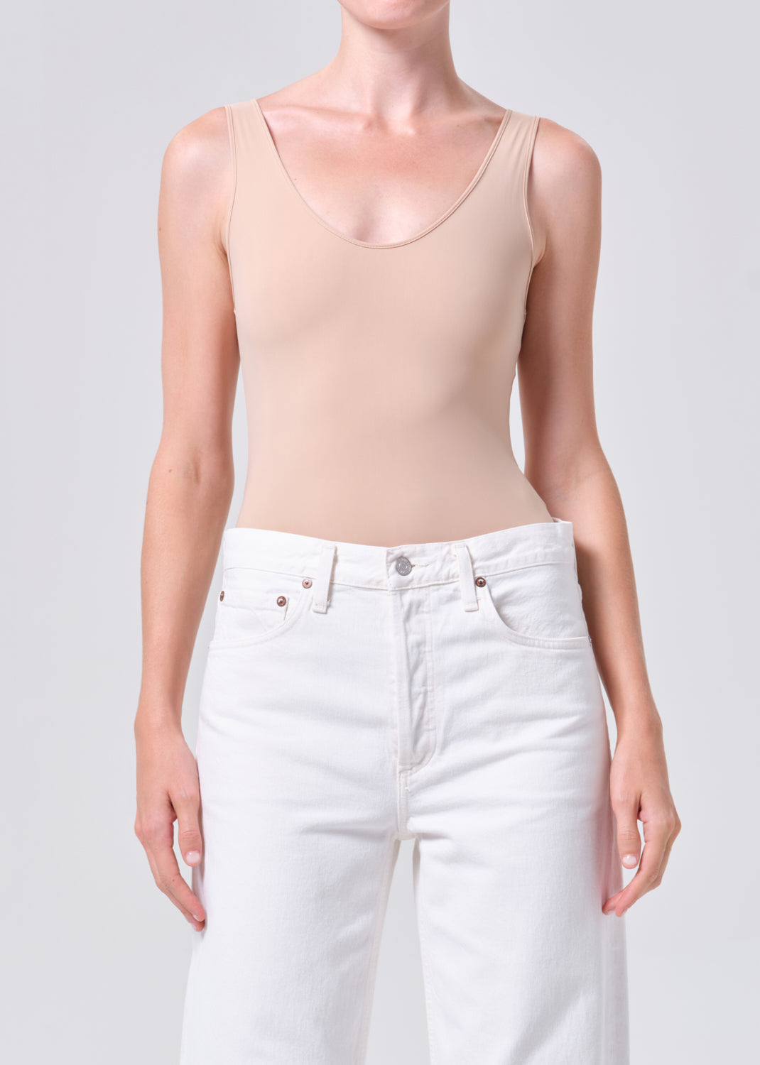 Person wearing a beige tank top and white pants on a plain background