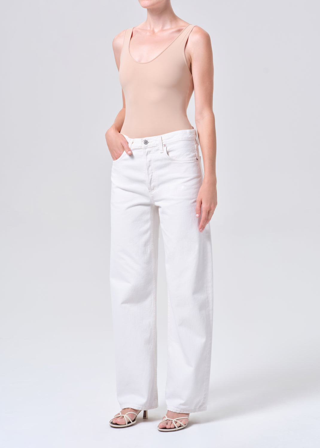 Person wearing a beige tank top and white pants on a plain background