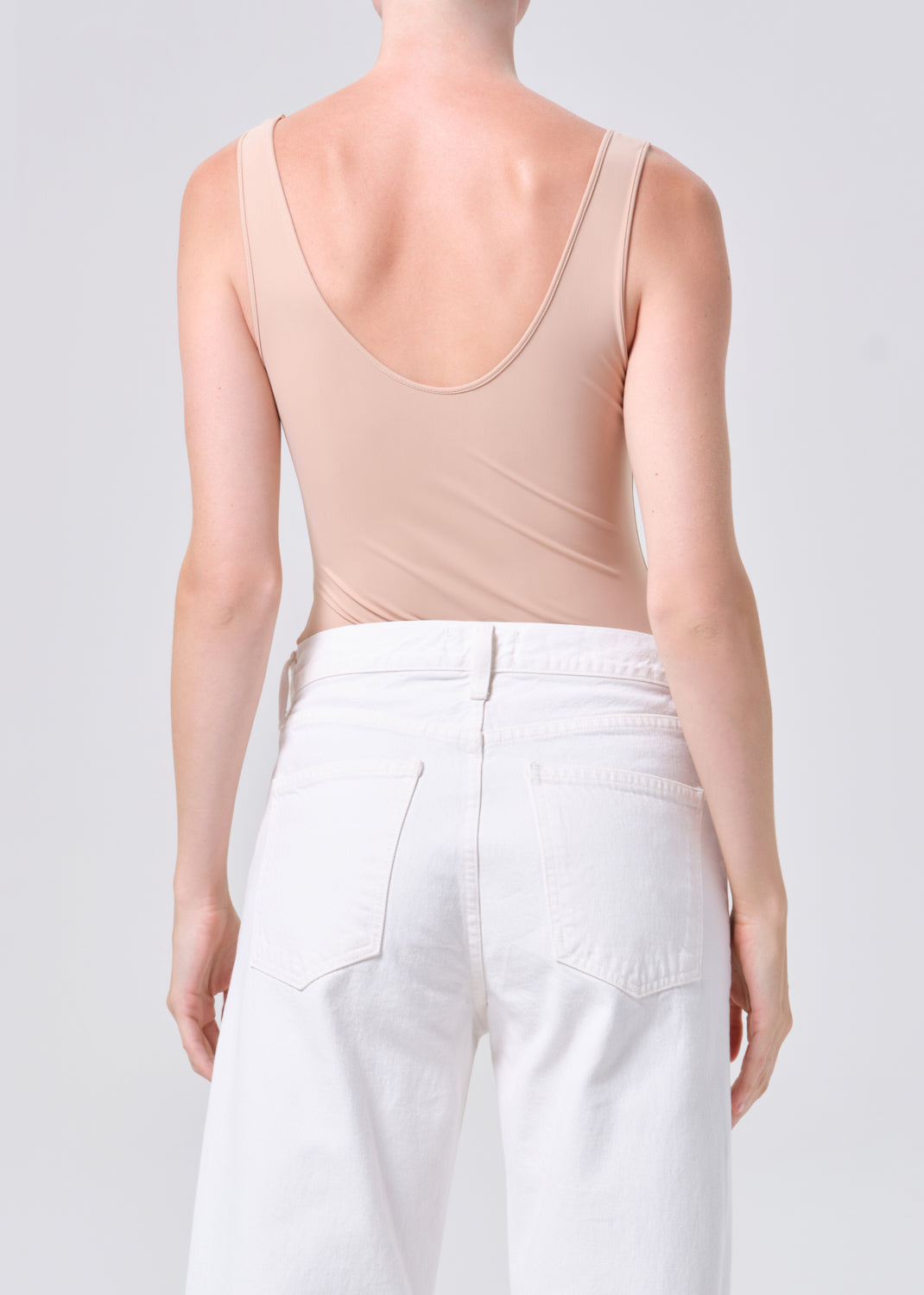 Person wearing a beige tank top and white pants on a plain background