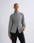 A model wearing a black and white vertically striped button-down shirt with black jeans, standing against a plain light gray studio background.