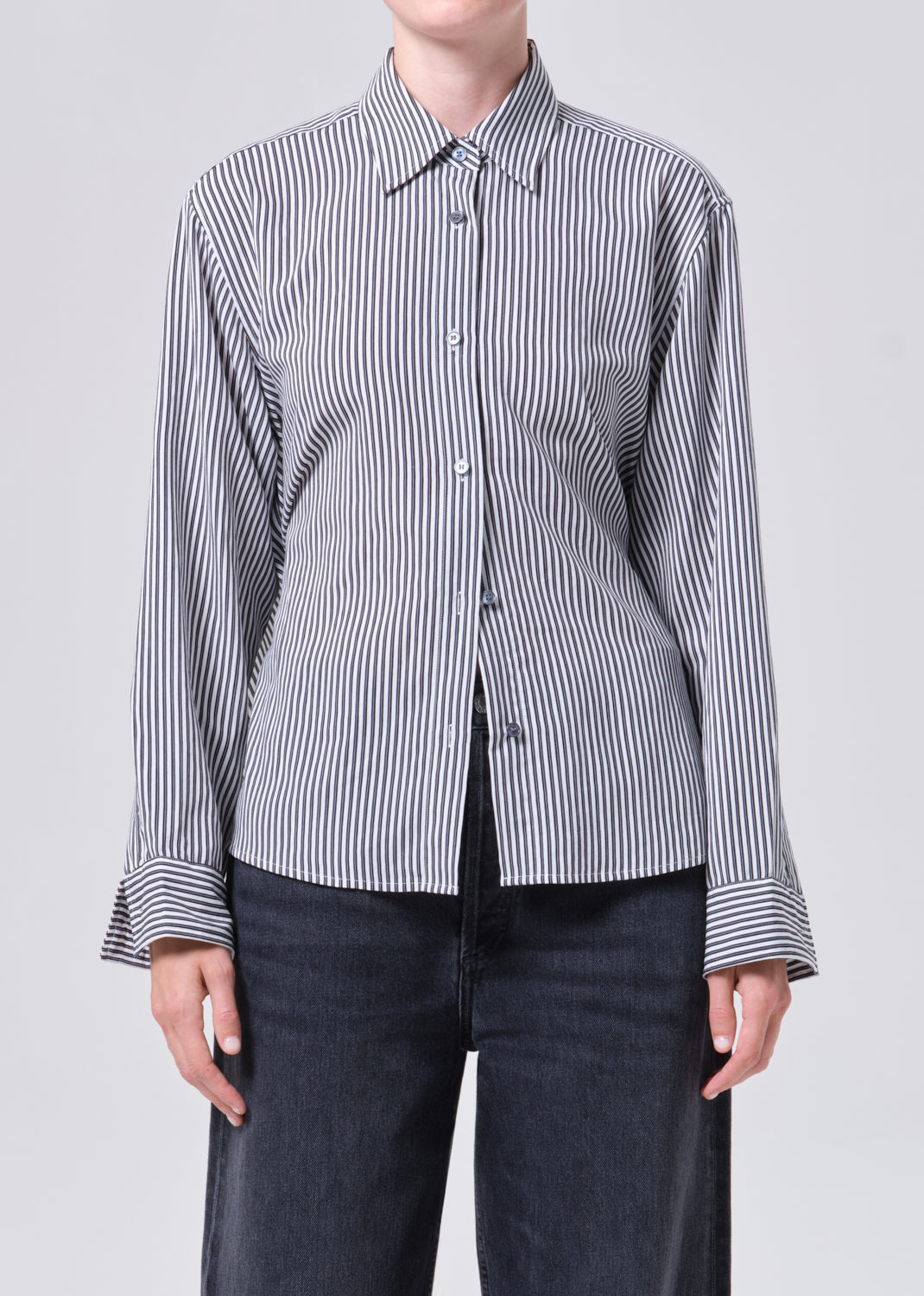 Person wearing a black and white striped shirt with rolled-up sleeves on a light gray background