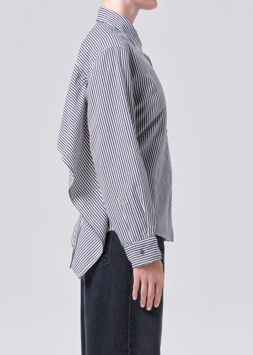 Person wearing a black and white striped shirt with an asymmetrical hem on a light gray background