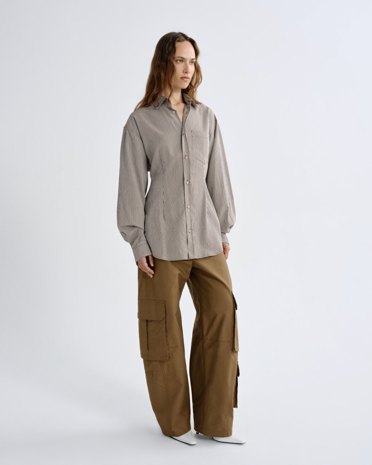 Person wearing a light gray shirt and brown cargo pants on a white background