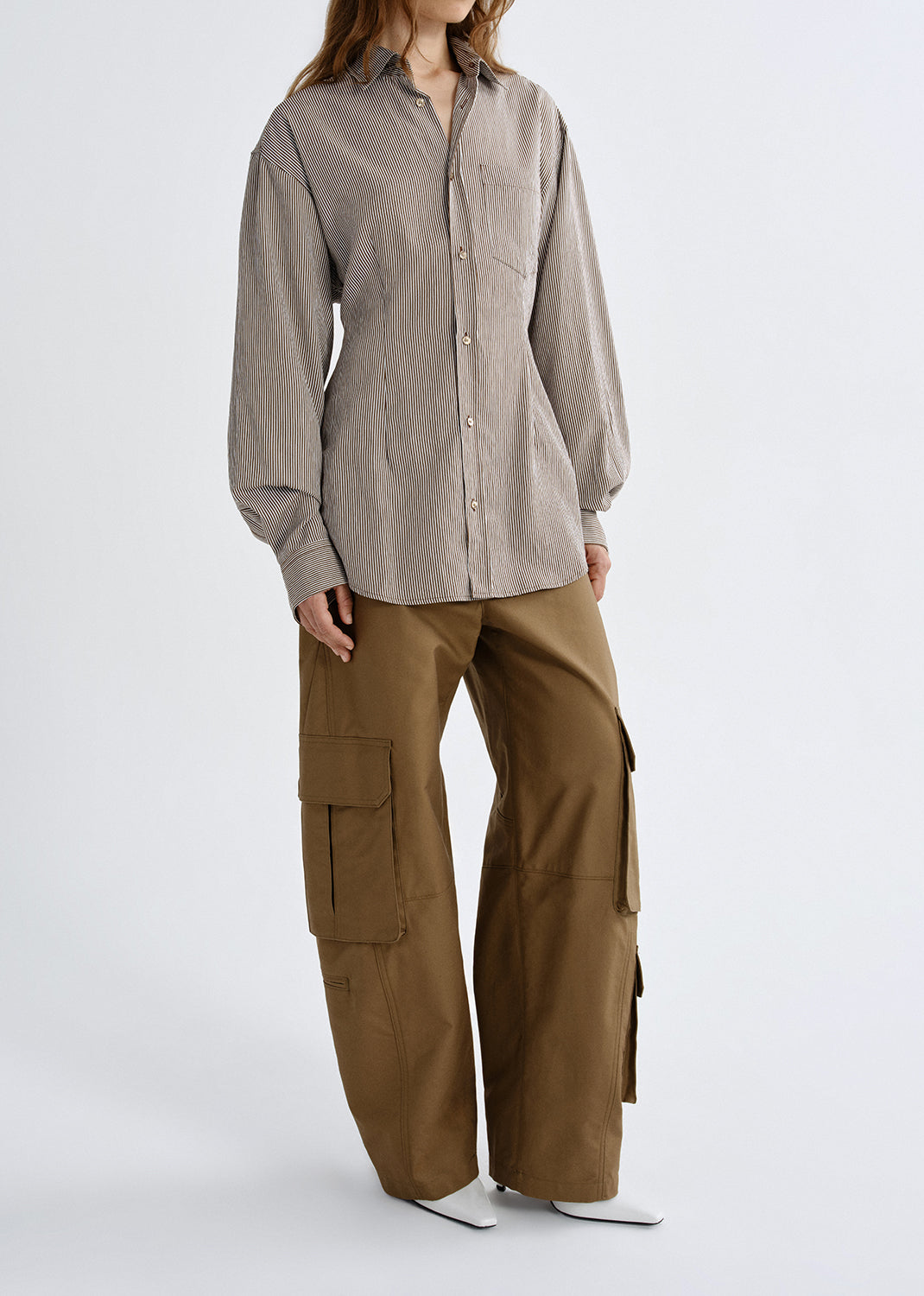 A model wearing a light taupe long-sleeve button-up shirt and wide-leg brown cargo pants, standing against a grey background.