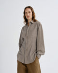 Person wearing a gray striped shirt and brown pants on a white background
