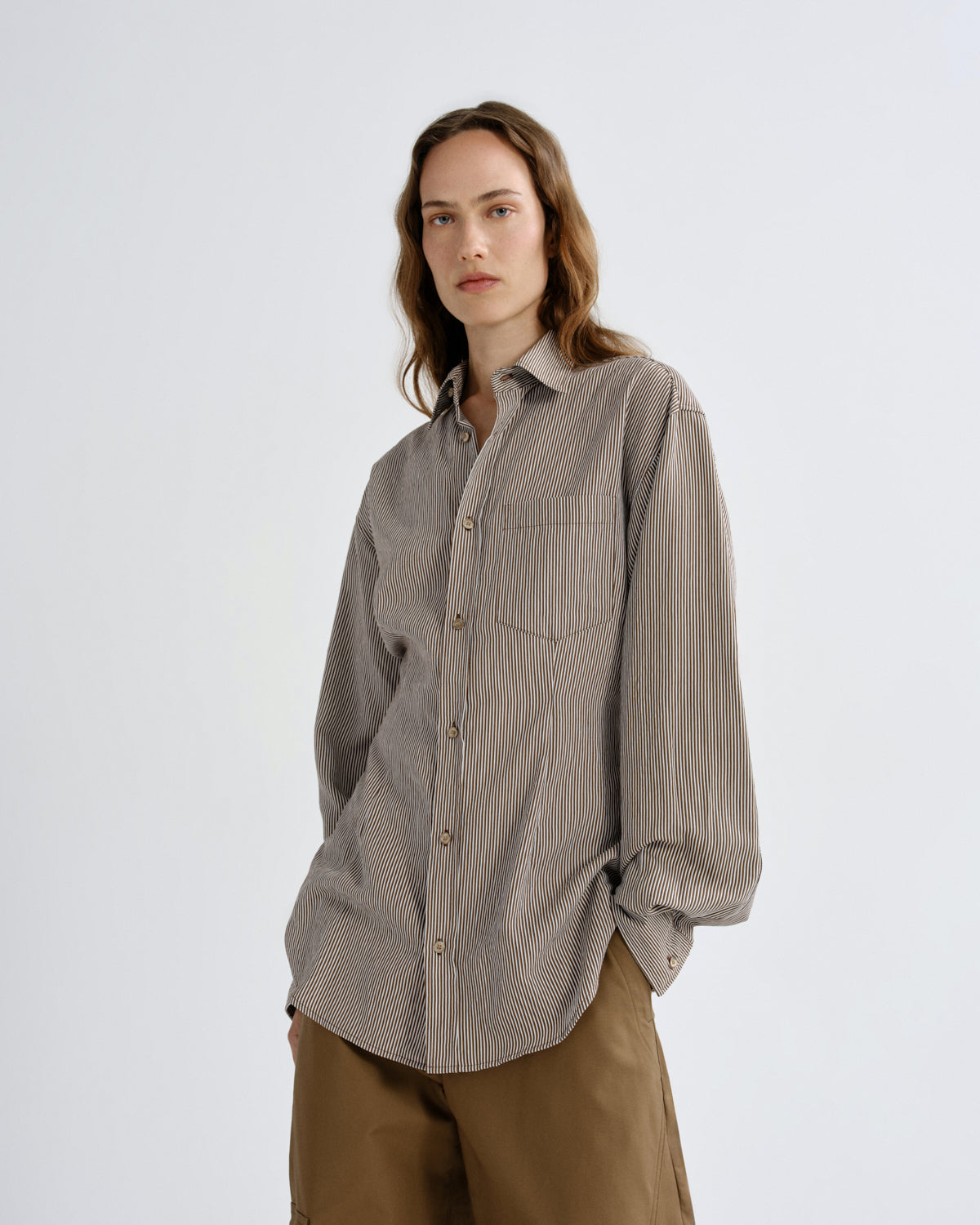 Person wearing a gray striped shirt and brown pants on a white background