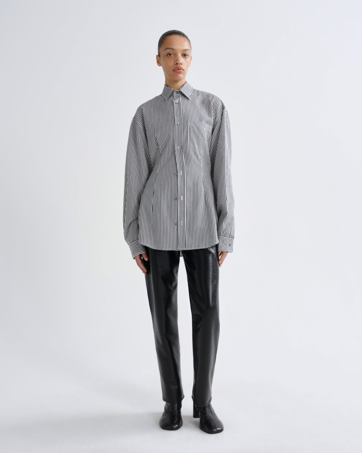 Person wearing a gray striped shirt and black pants on a white background