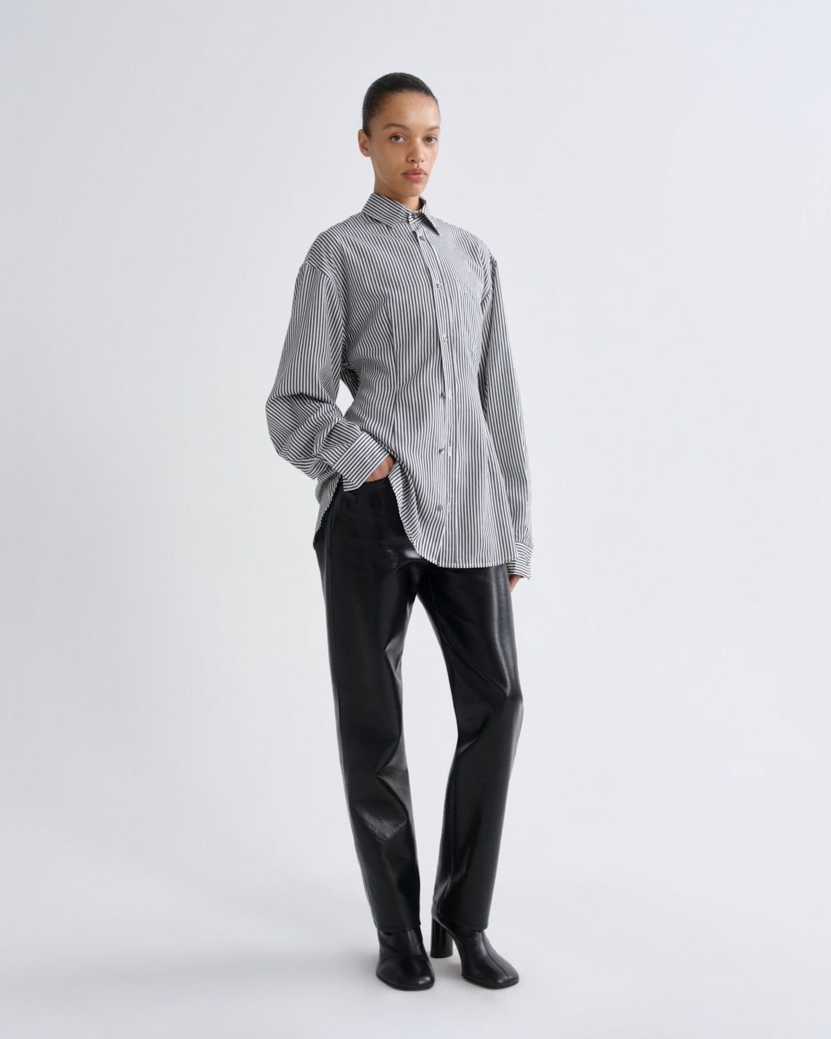 Person wearing a striped shirt and black pants on a white background