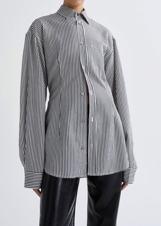 A person wearing an oversized black and white vertically striped button-up shirt with black pants, photographed against a grey background.