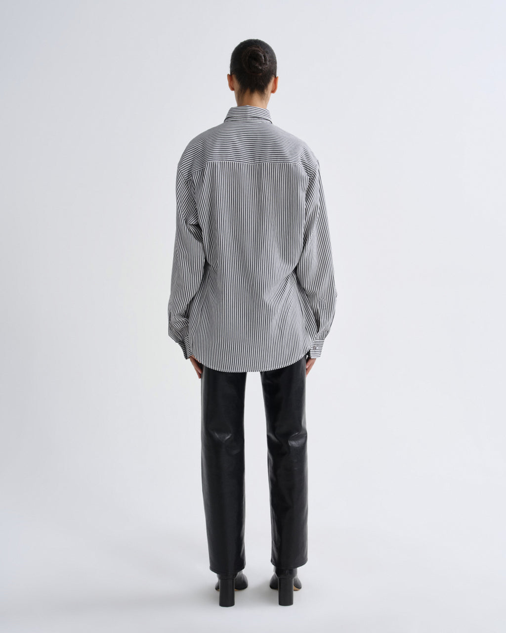 Person wearing a striped shirt and black pants on a white background