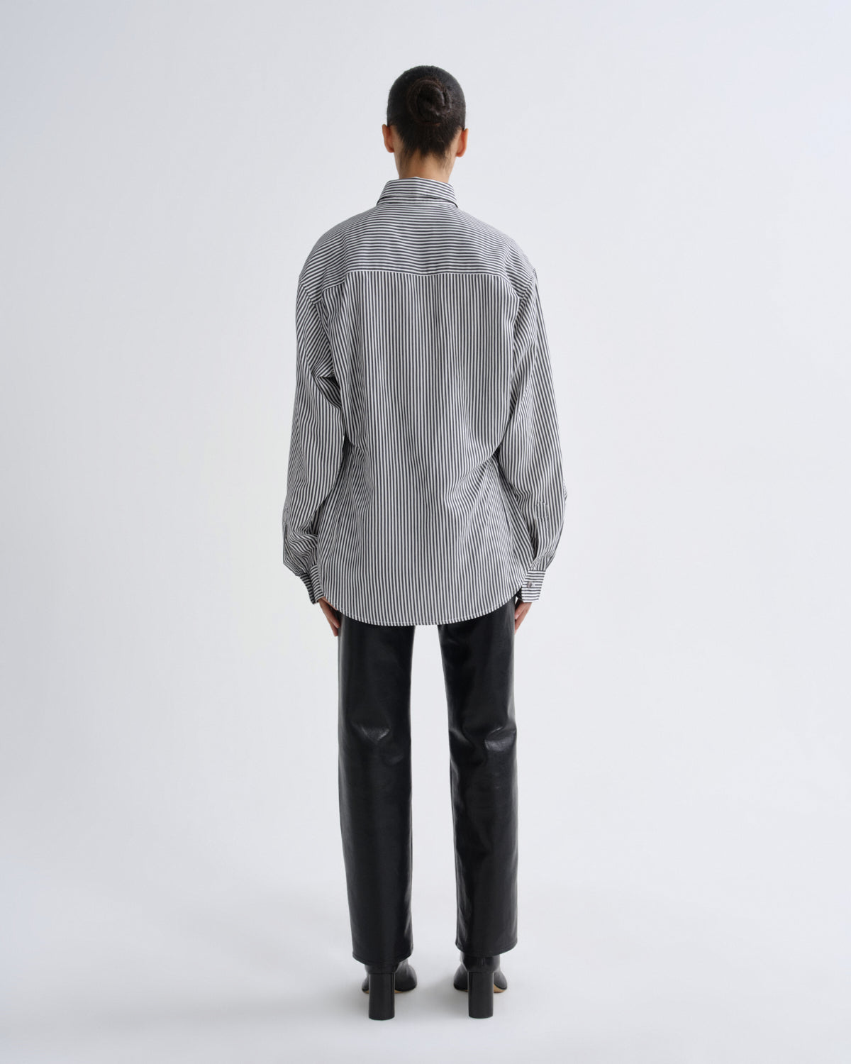 Person wearing a striped shirt and black pants on a white background