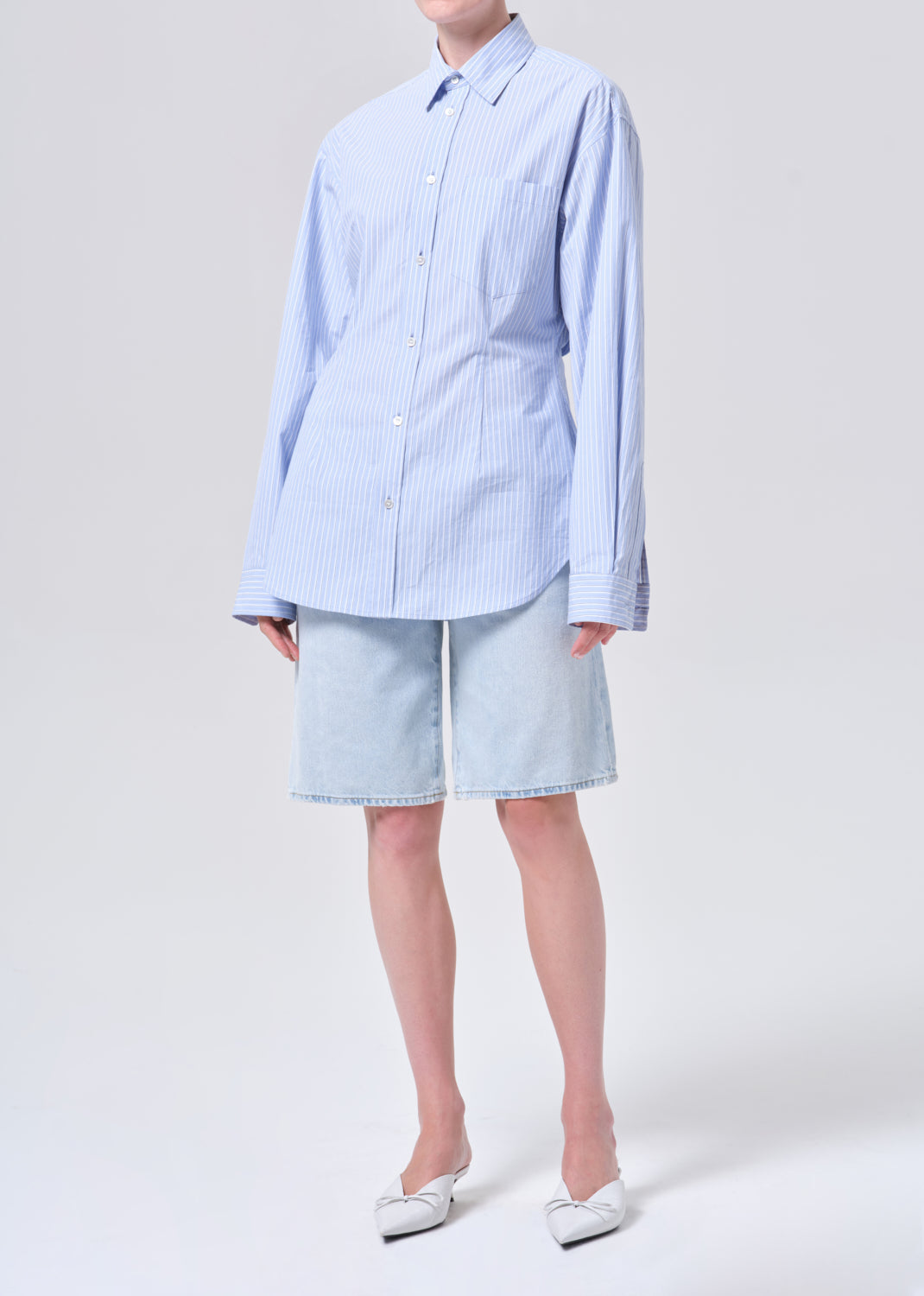 Person wearing a light blue checkered shirt and shorts on a white background