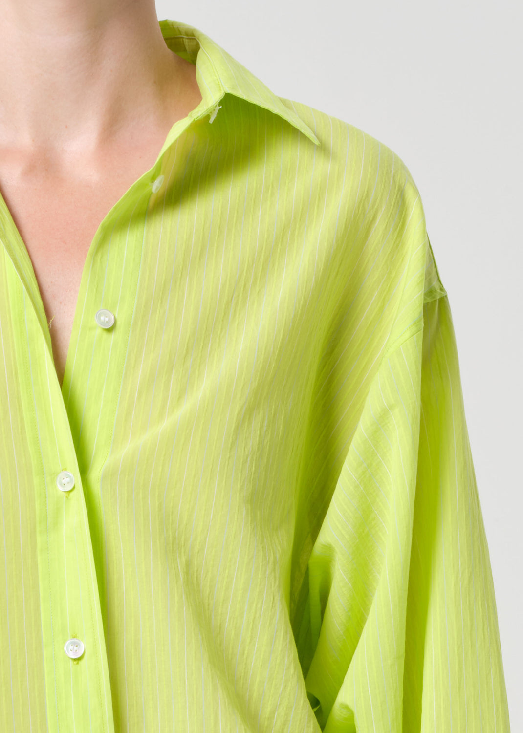 Close-up of a person wearing a light green shirt with a plain background