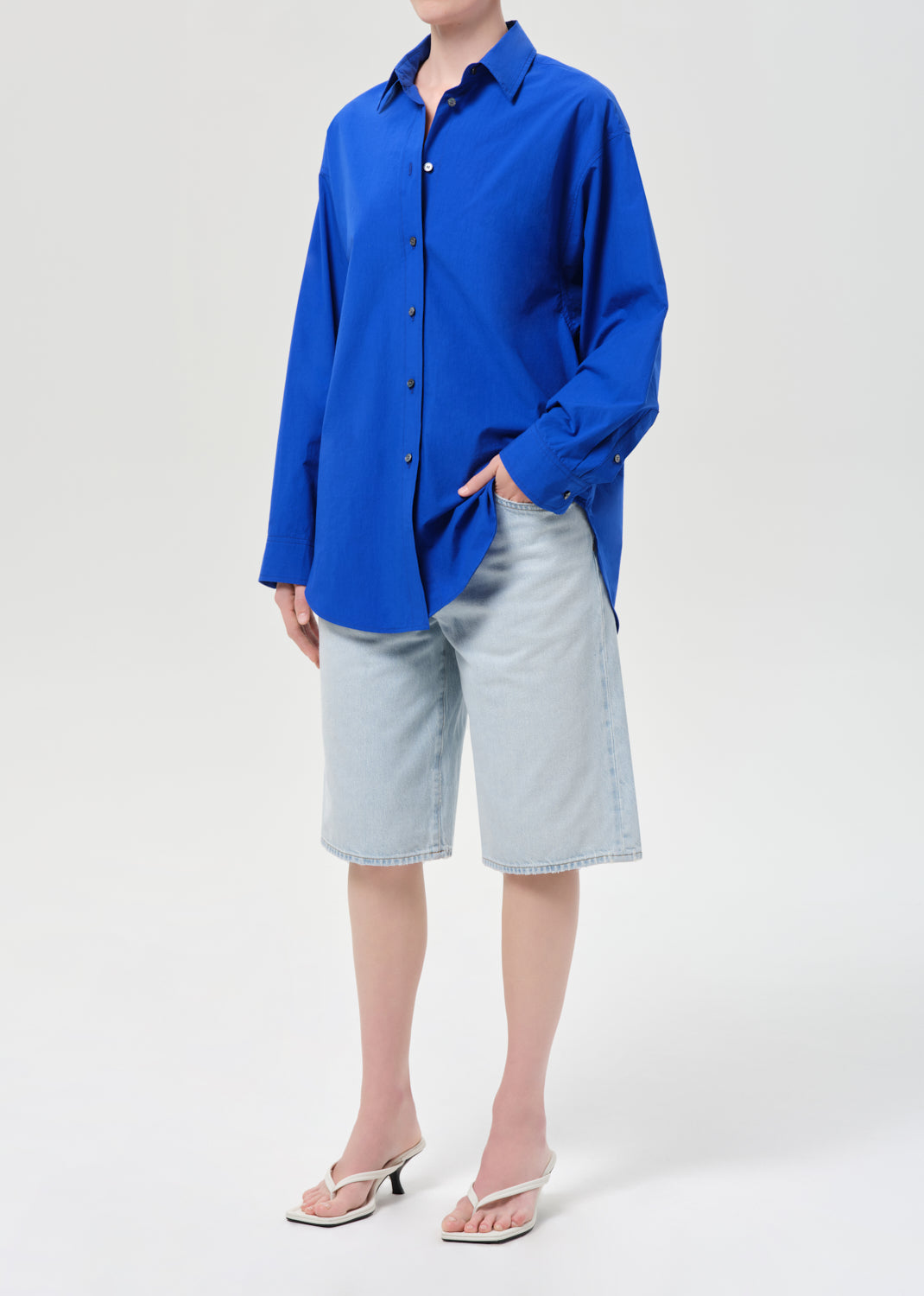 Person wearing a blue shirt and light gray shorts on a white background