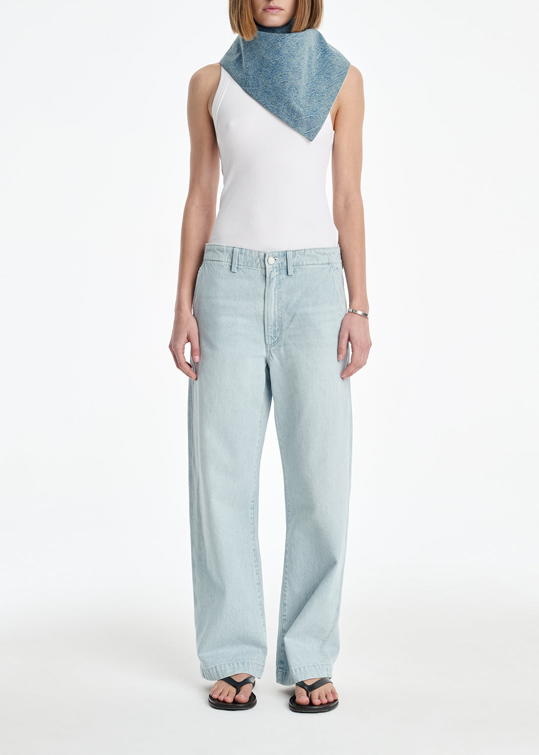 Woman wearing a white sleeveless top and light blue jeans with a denim scarf on a white background
