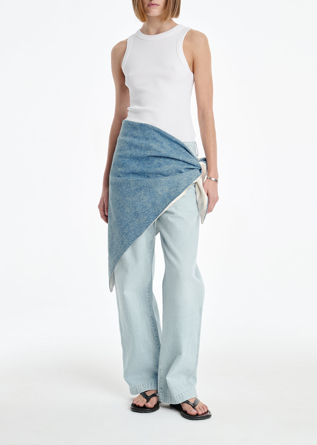 Woman wearing a white sleeveless top and light blue denim skirt on a white background