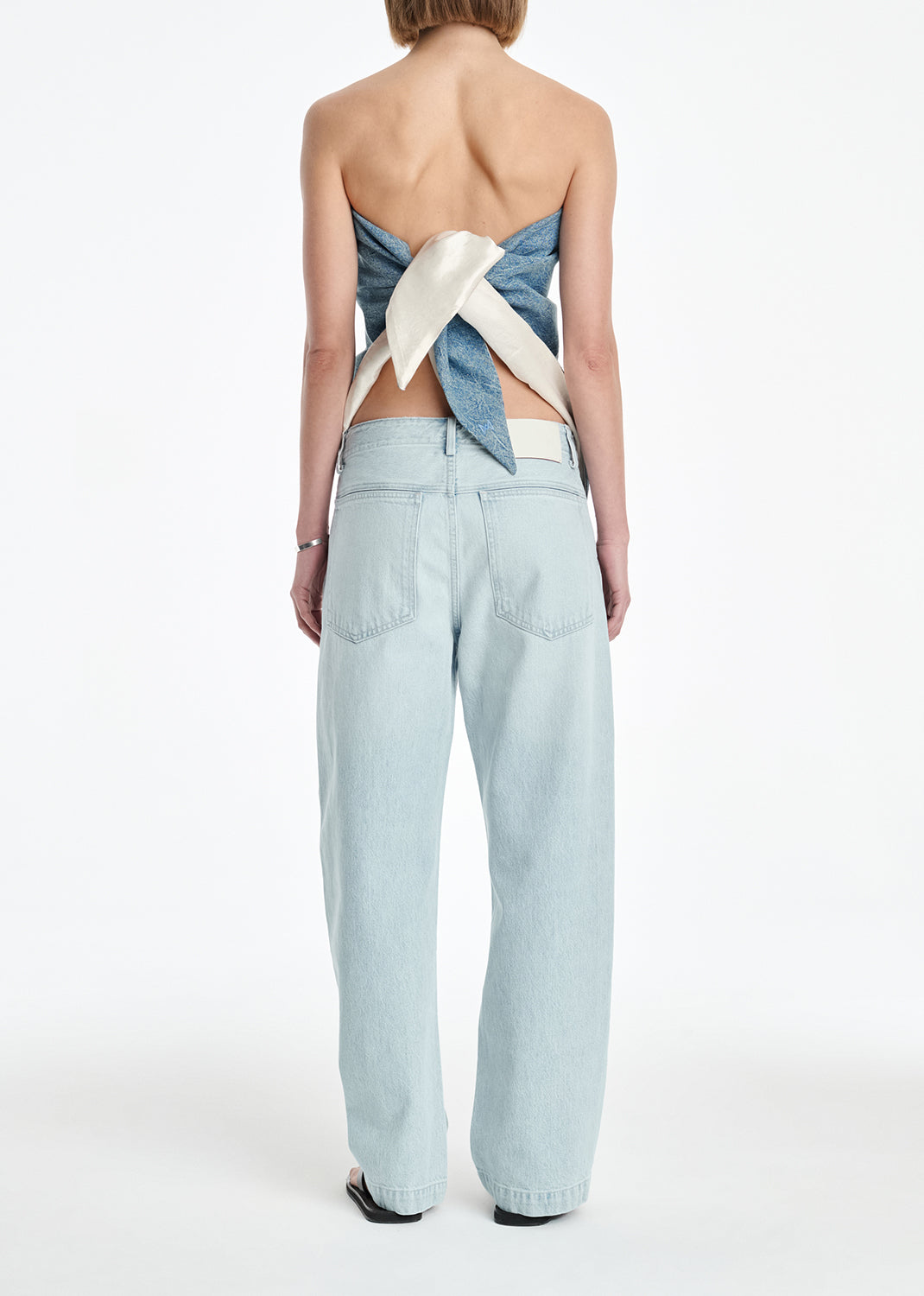 Person wearing light blue denim pants and a strapless top with a bow detail on a white background