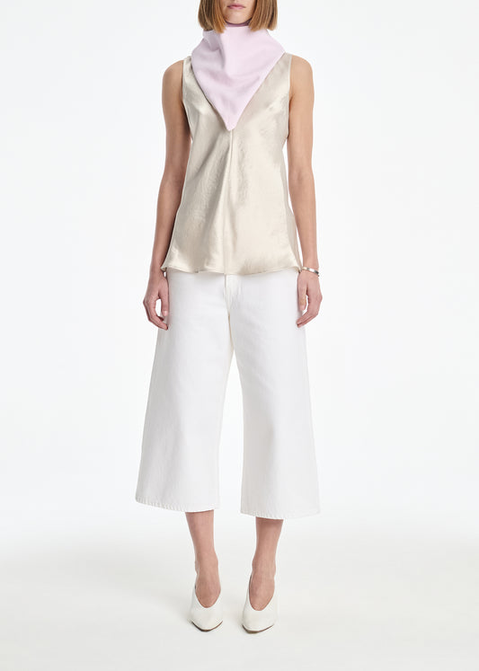 Woman wearing a sleeveless top and white pants with a pink scarf on a white background